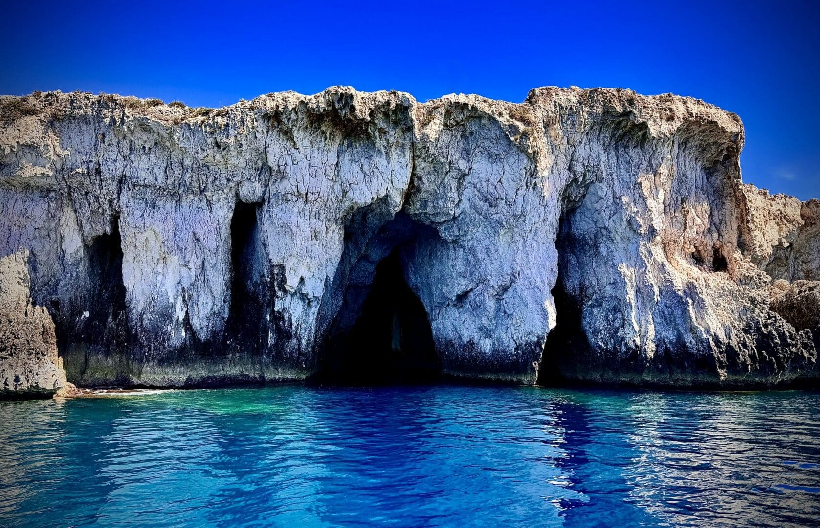 Rocky coastal cave with clear blue water.
